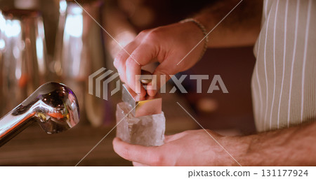 Bartender work. Bar ice cube. Male hand making stamp on frozen water figurine. Hot metal personalized business carving logo for drink. 131177924