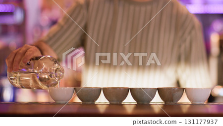 Oriental liquor. Bartender occupation. Man pouring rice wine sake from bottle to clay bowls. Barkeeper filling cups with asian alcoholic liquid. 131177937