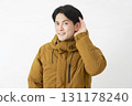A man wearing a down jacket listening carefully on a white background 131178240