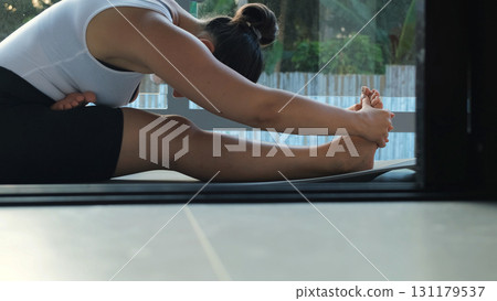 Woman stretching in morning light on balcony with palm trees, focusing on wellness and inner balance during her daily routine  131179537