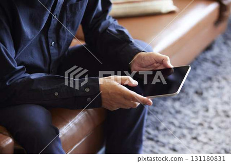 一位老年男子在家裡的沙發上進行線上學習。 一位老年男子在家裡的沙發上進行線上學習。 131180831