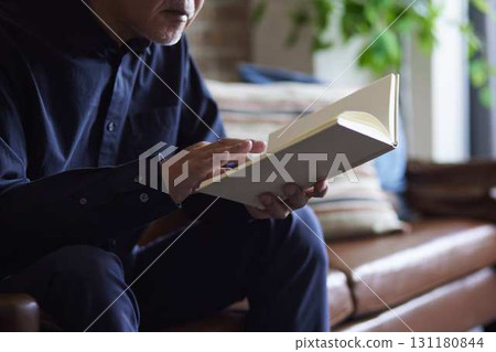 Senior Japanese man reading a book in the living room Senior Japanese man reading a book in the living room 131180844