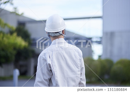 The back view of a senior male worker standing and gazing at the factory facilities. The back view of a senior male worker standing and gazing at the factory facilities. 131180884