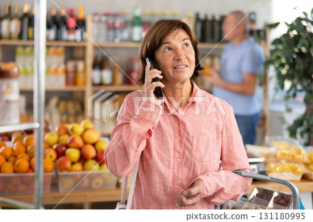 Elderly woman choosing groceries while talking on phone Elderly woman choosing groceries while talking on phone 131180995