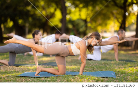 Girl doing balancing table pose during group yoga session in park 131181160