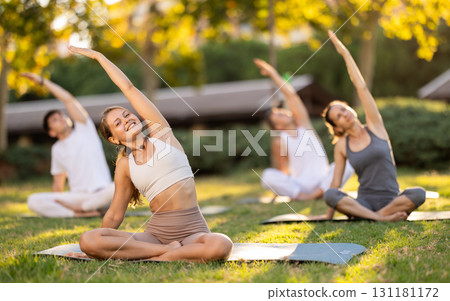 Girl performing stretches in lotus position during group yoga outdoors 131181172