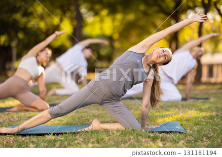 Yoga lesson visitors with girl coach perform Parighasana in park Yoga lesson visitors with girl coach perform Parighasana in park 131181194