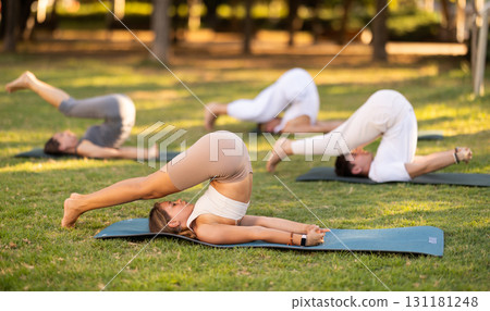 Young woman doing plow pose during group yoga in park 131181248