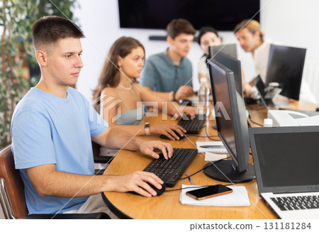 Guy student of computer courses looks at monitor screen, types on keyboard and does work 131181284