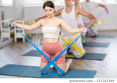 Young girl doing arm workout with resistance band standing on knees 131181344