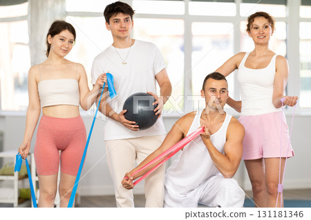 Young men and women posing together in training room holding resistance bands and pilates ball 131181346