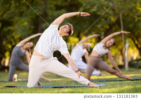 Yoga lesson visitors with guy coach perform Parighasana in park Yoga lesson visitors with guy coach perform Parighasana in park 131181363