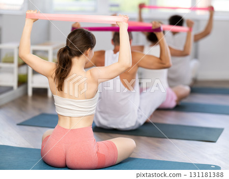 Young girl doing shoulder workout with resistance band sitting cross-legged 131181388