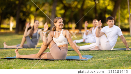 Girl performing twisting asana Matsyendrasana on green meadow 131181443