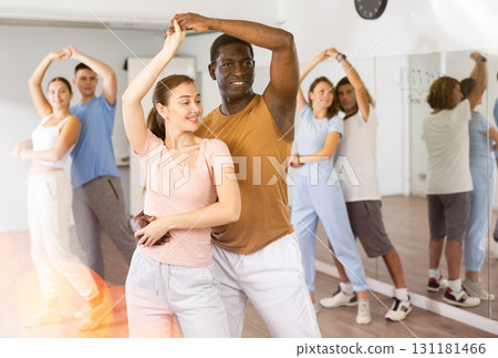 Positive smiling dancing couple enjoying active dancing during group training in dance hall Positive smiling dancing couple enjoying active dancing during group training in dance hall 131181466
