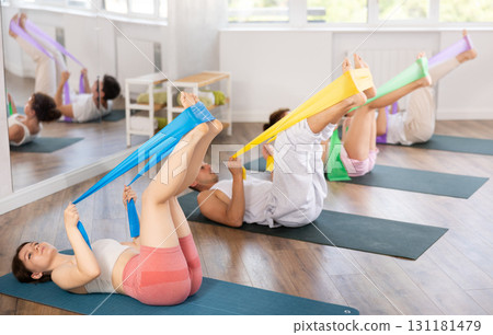 Young men and women practicing leg lift with band on knees lying on the side 131181479