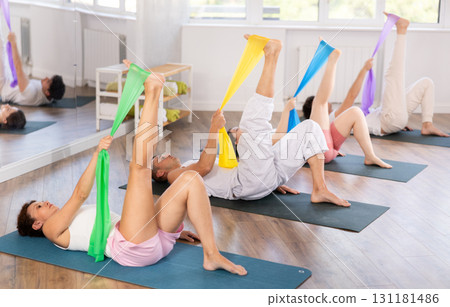 Young men and women practicing leg stretching with band lying back 131181486