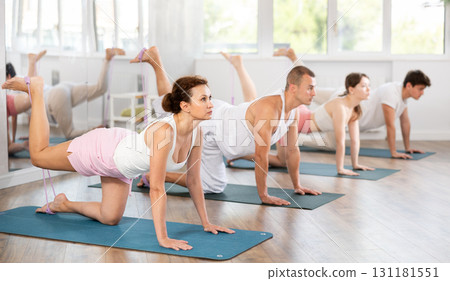 Young men and women practicing back leg lift with band standing on knees 131181551