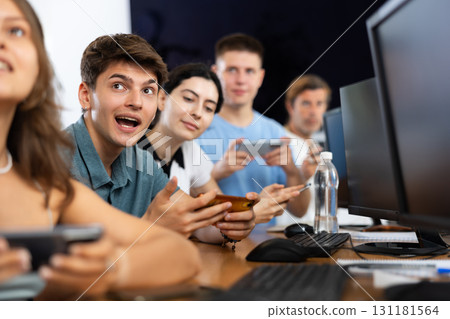 At computer class, young guy student sits with mobile phone and listens admiringly to teacher 131181564