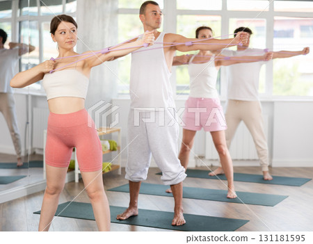Young men and women doing shoulder workout with resistance band in standing positions 131181595