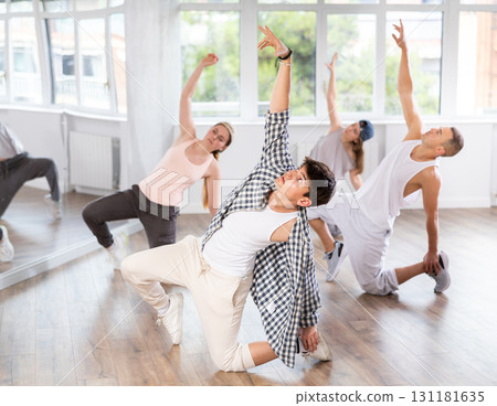 Man and his students perform hip hop dance on one bent leg, movement in horizontal plane near floor 131181635