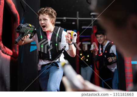 Emotional man with laser pistol playing laser tag with friends on dark labyrinth Emotional man with laser pistol playing laser tag with friends on dark labyrinth 131181663