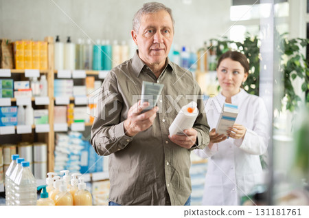 Senior man buys cream at drug store, girl pharmacist in background Senior man buys cream at drug store, girl pharmacist in background 131181761