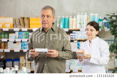 Elderly man chooses ointment in modern pharmacy. Female pharmacist helps with choosing medicine 131181826