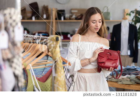 Happy young woman choosing handbag in clothing store Happy young woman choosing handbag in clothing store 131181828