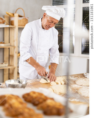 Experienced aged baker portioning dough on floured table 131181861