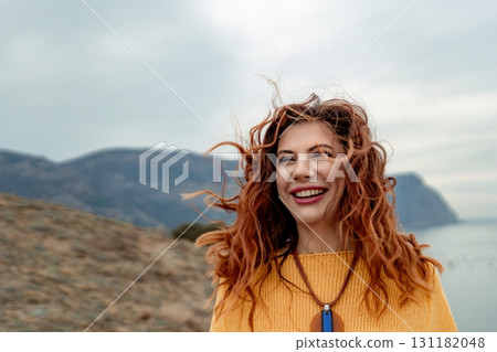 Portrait windswept hair happy woman against a backdrop of mountains and sea. Daylight illuminates the tranquil outdoor setting 131182048