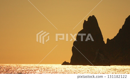 Sea rocks glittering ocean sunset: Coastal cliffs darken as golden sun reflects on sea, creating scenic vista. Sea rocks glittering ocean sunset: Coastal cliffs darken as golden sun reflects on sea, creating scenic vista. 131182122