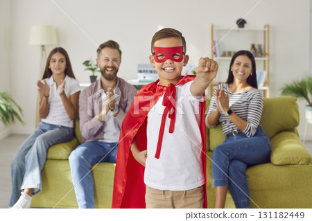 Happy smiling child boy in superhero costume standing at home with his family in background. Happy smiling child boy in superhero costume standing at home with his family in background. 131182449