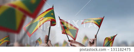 Grenada flags in their hands on a blurred urban background Grenada flags in their hands on a blurred urban background 131182475