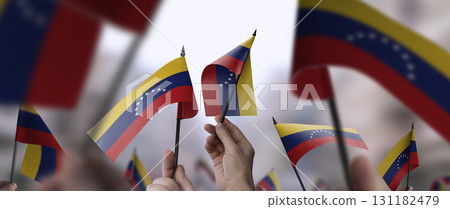 Venezuela flags in their hands on a blurred urban background 131182479