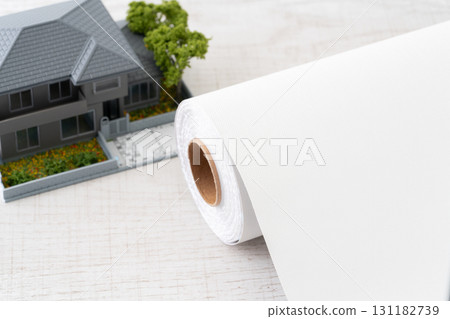 Close-up of a miniature house and a roll of white wallpaper sheets 131182739