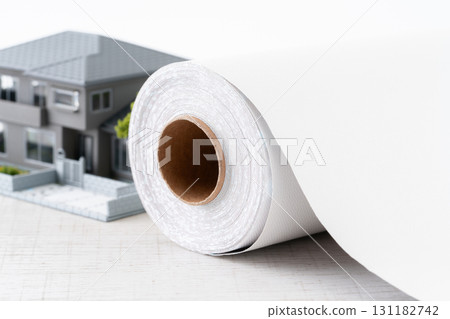 Close-up of a miniature house and a roll of white wallpaper sheets 131182742