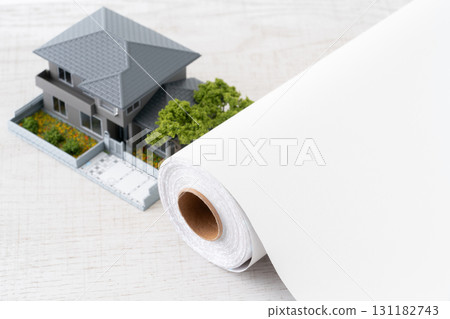 Close-up of a miniature house and a roll of white wallpaper sheets 131182743