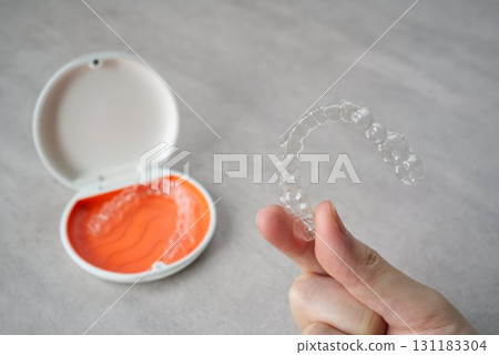 Hand holding orthodontic aligner with orange and white case Hand holding orthodontic aligner with orange and white case 131183304