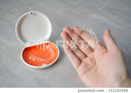 Hand holding orthodontic aligner with orange and white case Hand holding orthodontic aligner with orange and white case 131183309