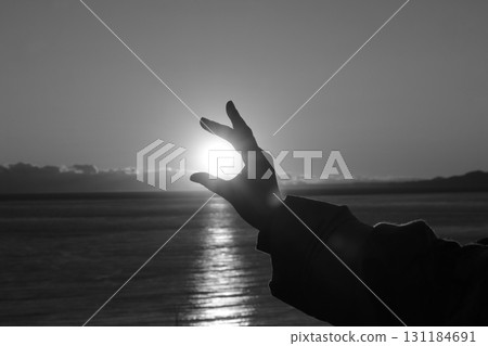 Silhouette of a person holding the setting sun with their hands 131184691