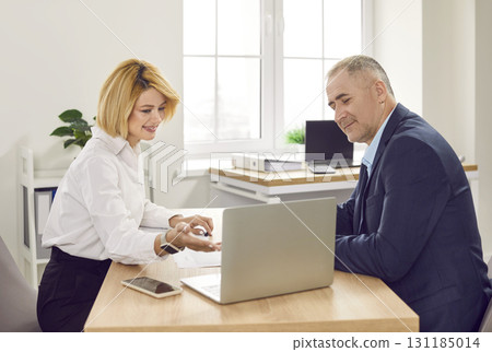 Smiling woman consultant and client sitting at desk using laptop discussing financial report Smiling woman consultant and client sitting at desk using laptop discussing financial report 131185014