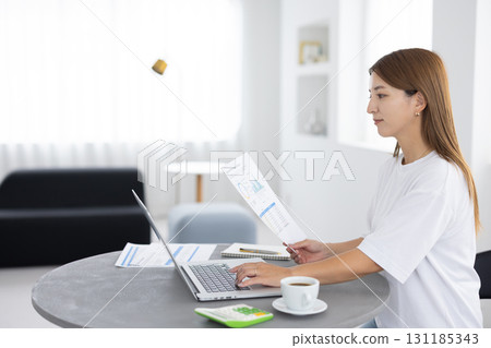 A woman working on a computer while looking at documents A woman working on a computer while looking at documents 131185343