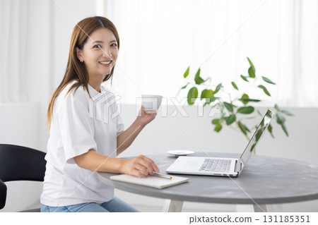 一位女士一邊喝咖啡一邊使用電腦 131185351