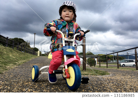 <Material> A smiling child riding a tricycle in the park 131186985