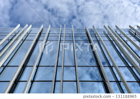 Skyscraper glass window facade against blue sky, clouds reflecting on windows Skyscraper glass window facade against blue sky, clouds reflecting on windows 131188965