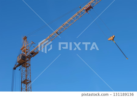 Moving yellow tower crane on construction site on blue sky background. Moving yellow tower crane on construction site on blue sky background. 131189136