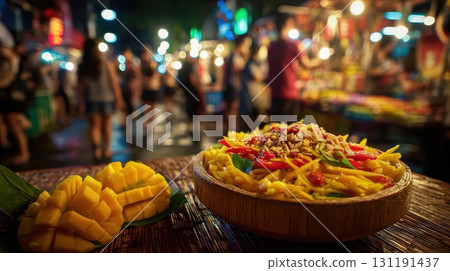 An immersive shot of a Thai mango salad with peanuts and mango pieces in the foreground, set against a vibrant night market 131191437