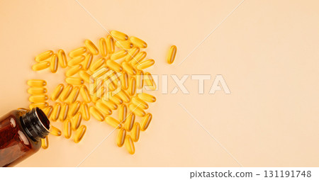 Fish oil softgels spilled from an amber bottle on a beige background with copy space 131191748