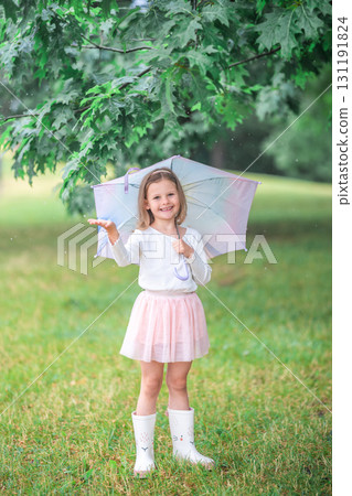 Little girl looking into the camera with joyful eyes while catching raindrops under an umbrella. Engaging with the moment and enjoying the rain through spontaneous play. Little girl looking into the camera with joyful eyes while catching raindrops under an umbrella. Engaging with the moment and enjoying the rain through spontaneous play. 131191824